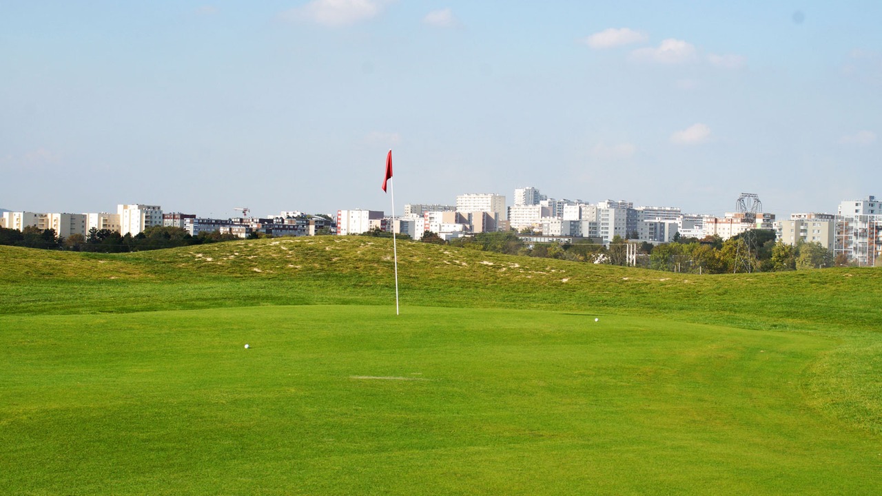 Green avec drapeau rouge et immeubles en arrière-plan au golf de Reims Bezannes
