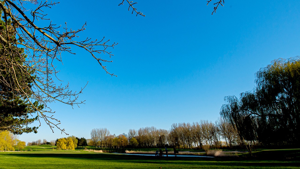 Parcours du Golf de Dunkerque bordé d’arbres et d’un plan d’eau sous un ciel bleu.