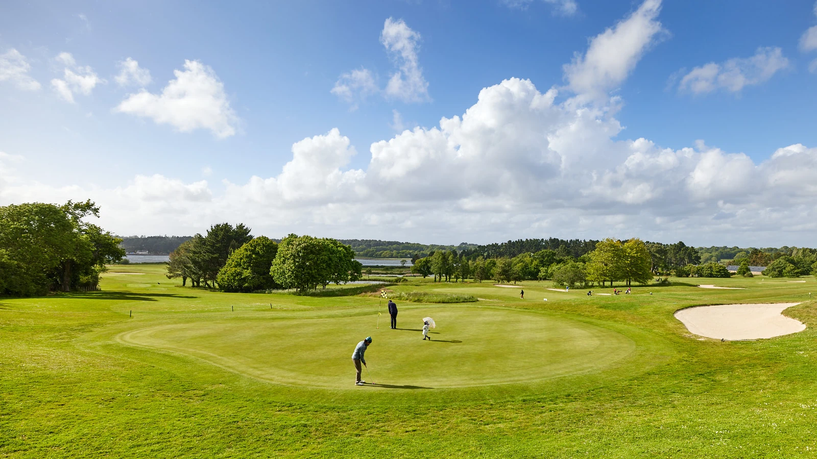 Golfeurs sur un green bordé d’un bunker, avec arbres et rivière au Golf Bluegreen Baden.