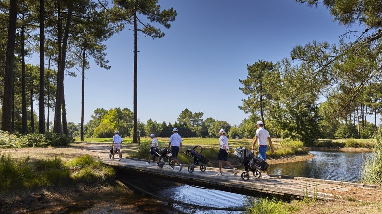 Golfeurs avec chariots traversant un pont sur un plan d’eau au Golf de Gujan-Mestras.