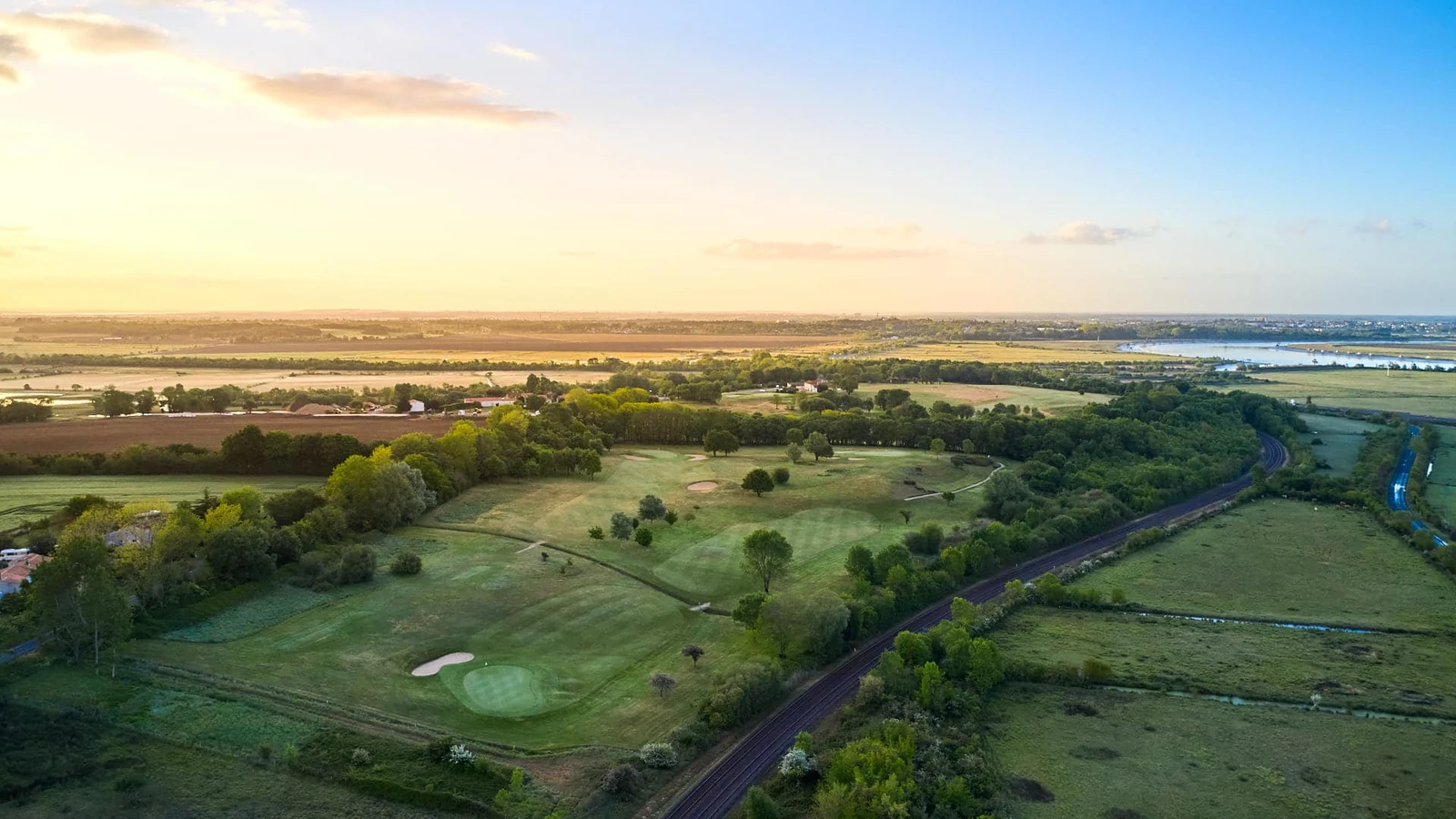 Vue aérienne des greens, bunkers et fairways du Golf Bluegreen Rochefort Océan au soleil couchant.