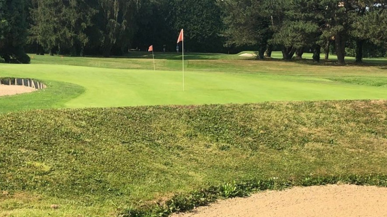 Green du Golf Club de Valenciennes avec drapeaux, bunkers et arbres autour du parcours.