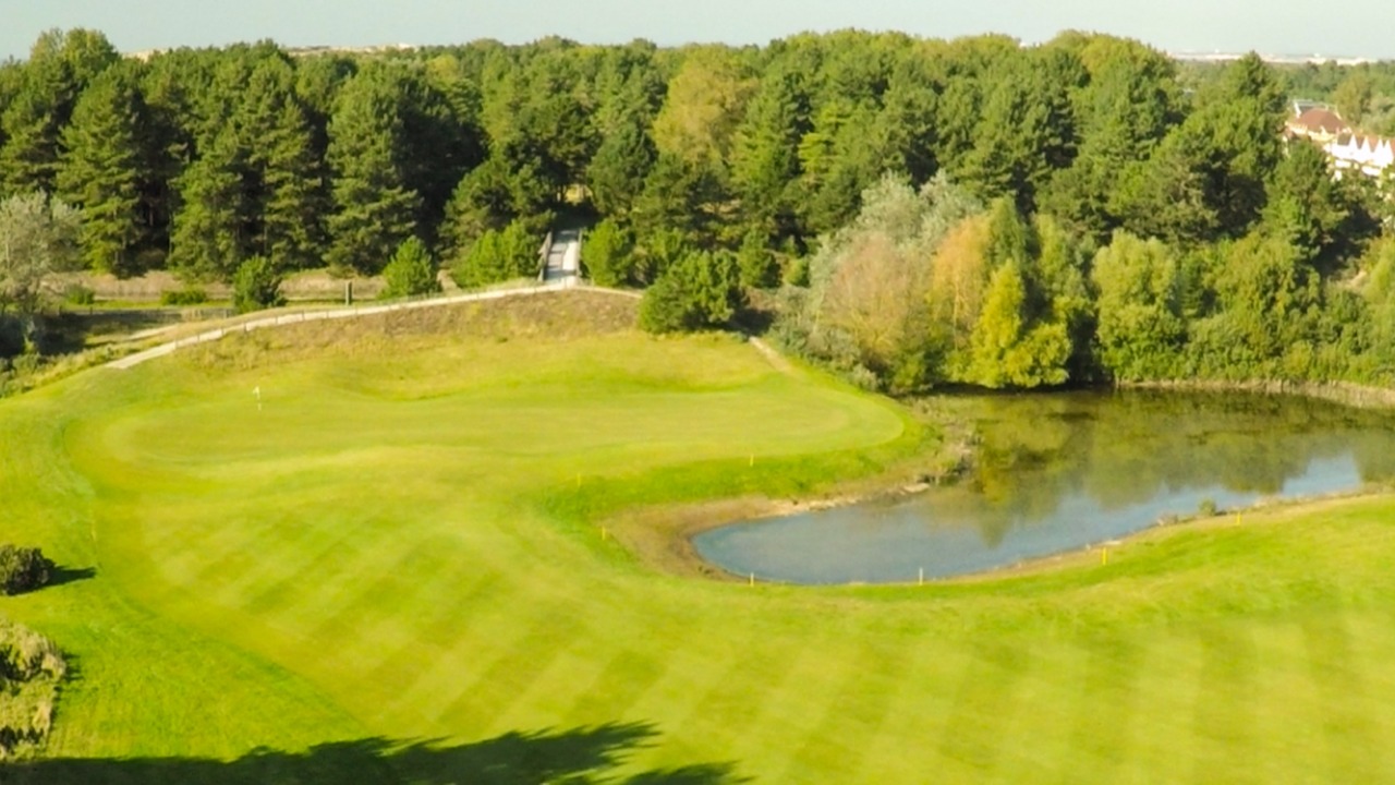 Vue aérienne d’un green bordé d’un plan d’eau et d’arbres au Golf de Belle Dune.