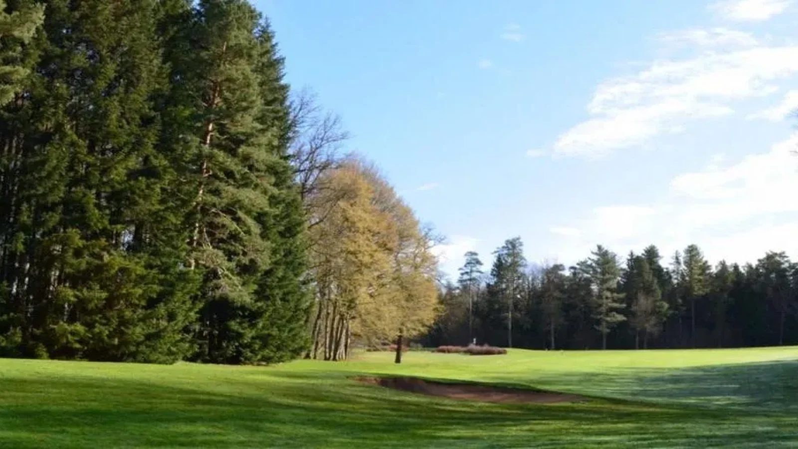 Fairway bordé de bois, bunker au premier plan et ouverture lumineuse ; pas de bâtiment dominant. Photographie finale inspectée sur la planche contact : pas de texte superposé ni filigrane visible ; recadrage non destructif et sujet golf représentatif. Identité exacte étayée par la page officielle, non inférée des pixels seuls. — Golf de Besançon