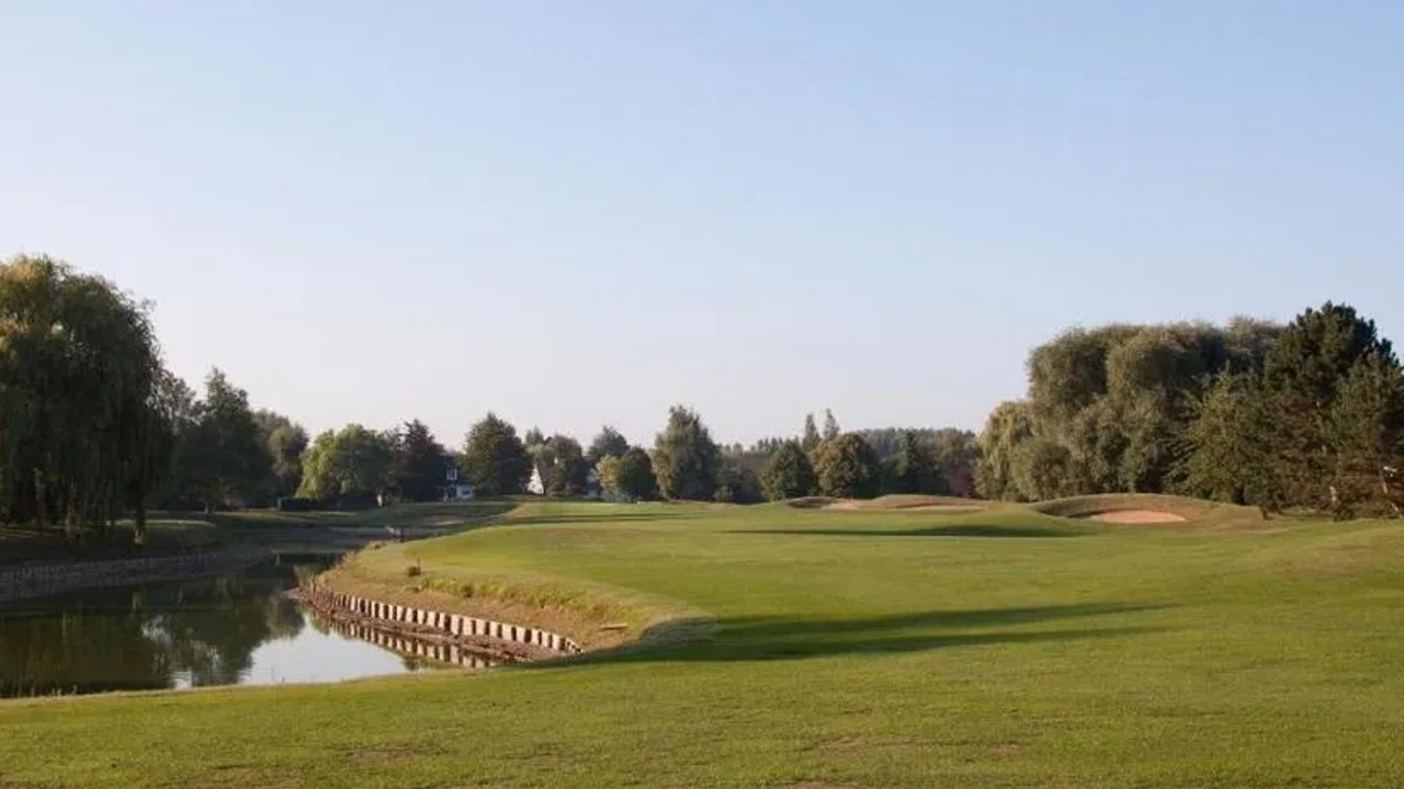 Parcours du Golf de Bondues avec plan d’eau à gauche, bunkers à droite et arbres en arrière-plan.