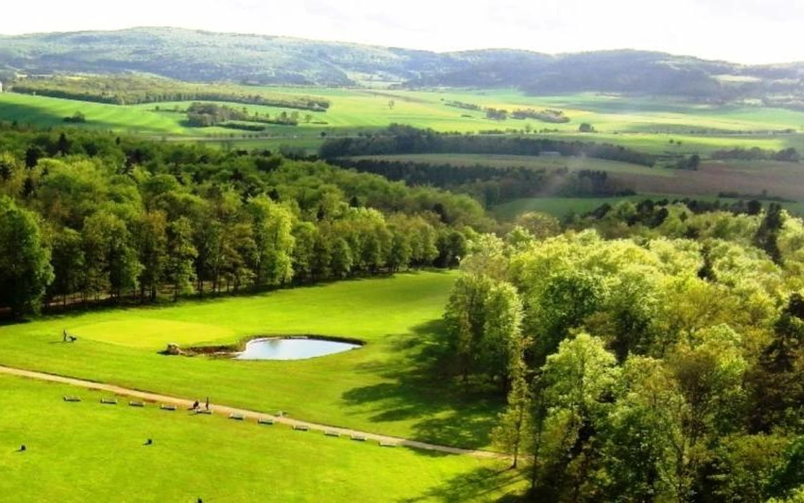 Vue aérienne du parcours vallonné, des bois et d’un plan d’eau. — Golf de la Chassagne