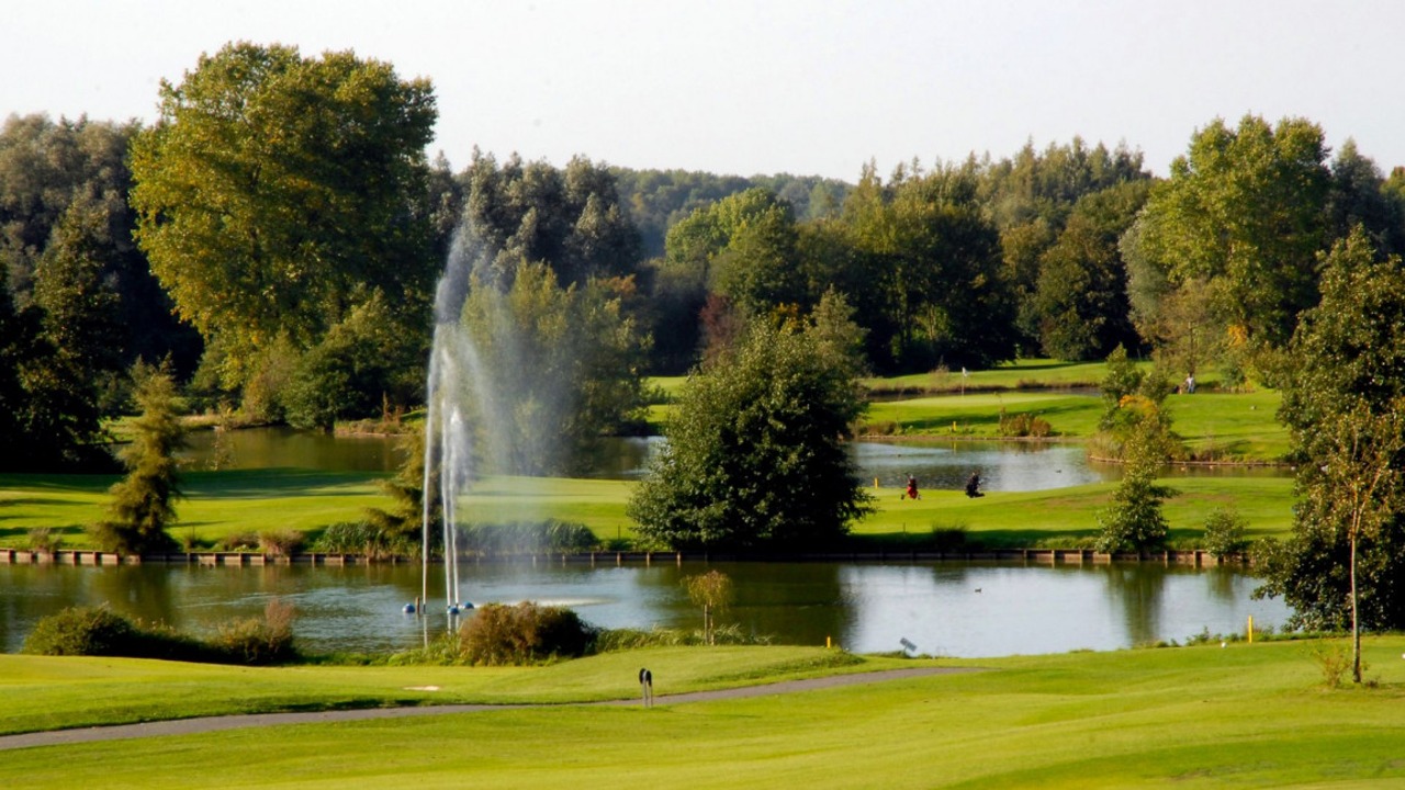 Parcours du Golf de Mormal entre étangs, jet d’eau et arbres, avec un green au second plan.