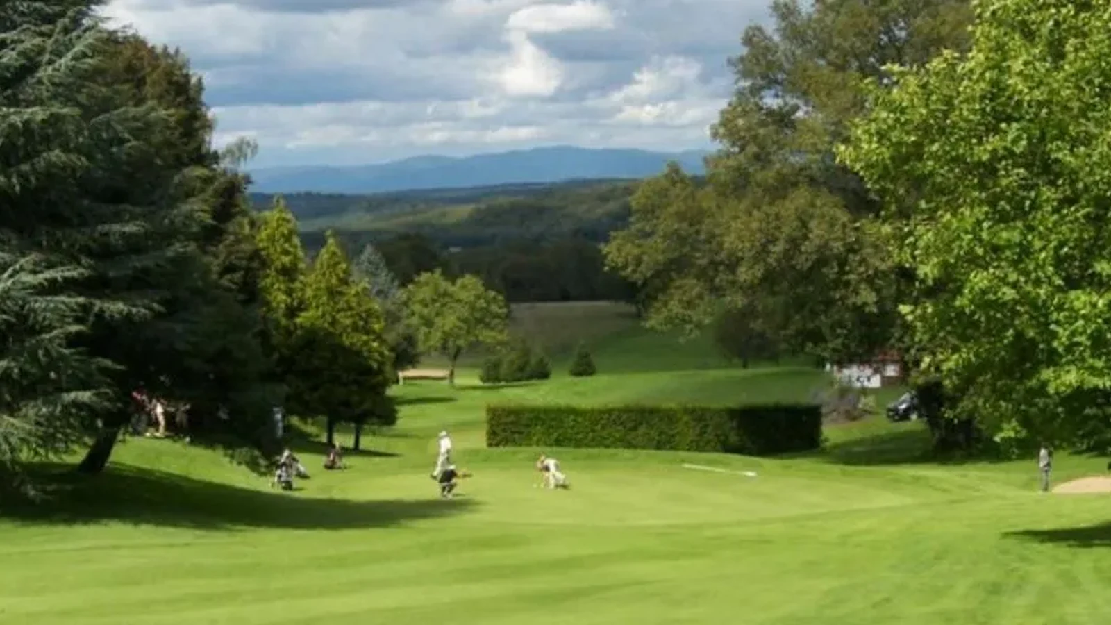 Fairway descendant avec petits groupes de joueurs, arbres et horizon vallonné. Photographie finale inspectée sur la planche contact : pas de texte superposé ni filigrane visible ; recadrage non destructif et sujet golf représentatif. Identité exacte étayée par la page officielle, non inférée des pixels seuls. — Golf de Prunevelle