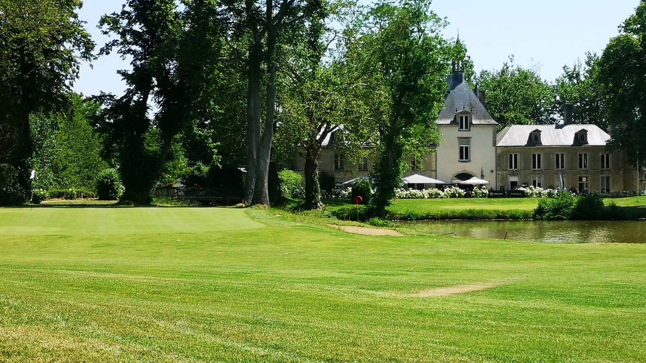 Green du Golf de Reims avec arbres, plan d’eau et château à l’arrière-plan.