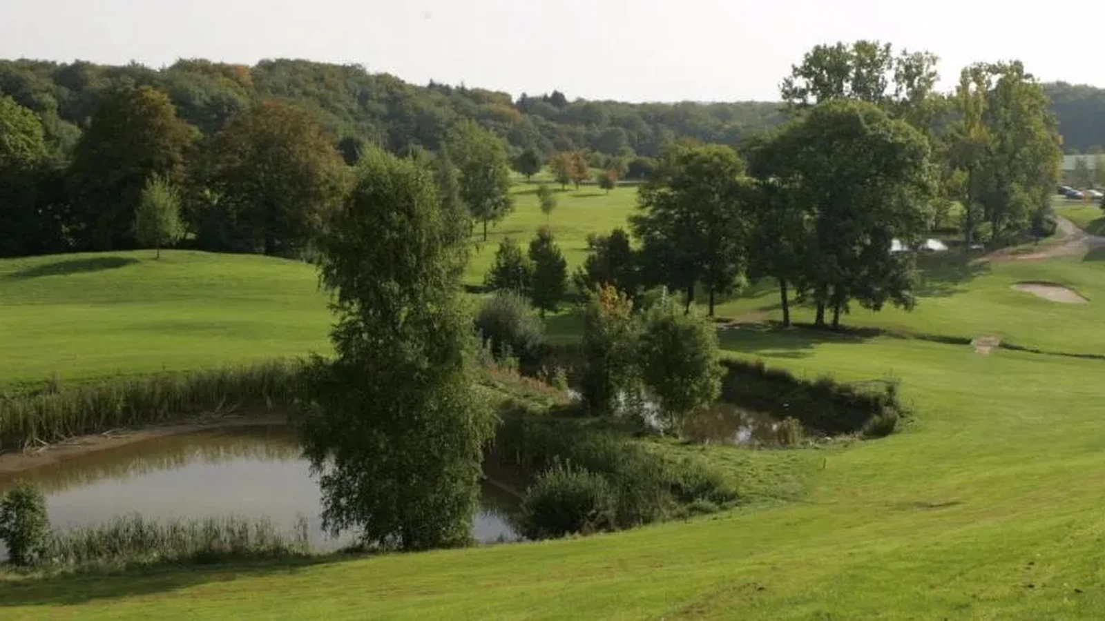 Vue du parcours arboré, obstacle d’eau et bunkers à droite ; composition représentative du golf. Photographie finale inspectée sur la planche contact : pas de texte superposé ni filigrane visible ; recadrage non destructif et sujet golf représentatif. Identité exacte étayée par la page officielle, non inférée des pixels seuls. — Golf de Rougemont-le-Château
