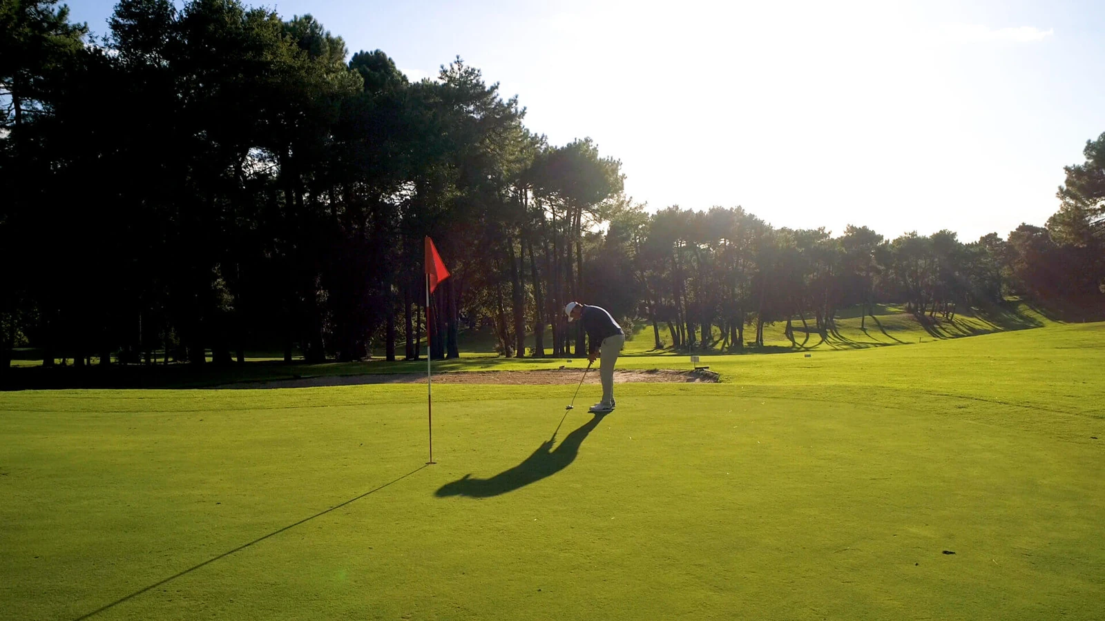 Green avec drapeau rouge, golfeur au loin et pins au Golf de Royan.