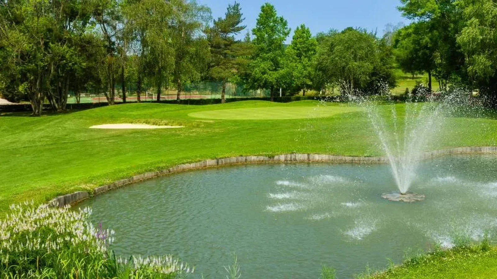 Green et bunker au-delà d’un obstacle d’eau avec jet ; golf lisible autour de la pièce d’eau. Photographie finale inspectée sur la planche contact : pas de texte superposé ni filigrane visible ; recadrage non destructif et sujet golf représentatif. Identité exacte étayée par la page officielle, non inférée des pixels seuls. — Golf du Val de Sorne