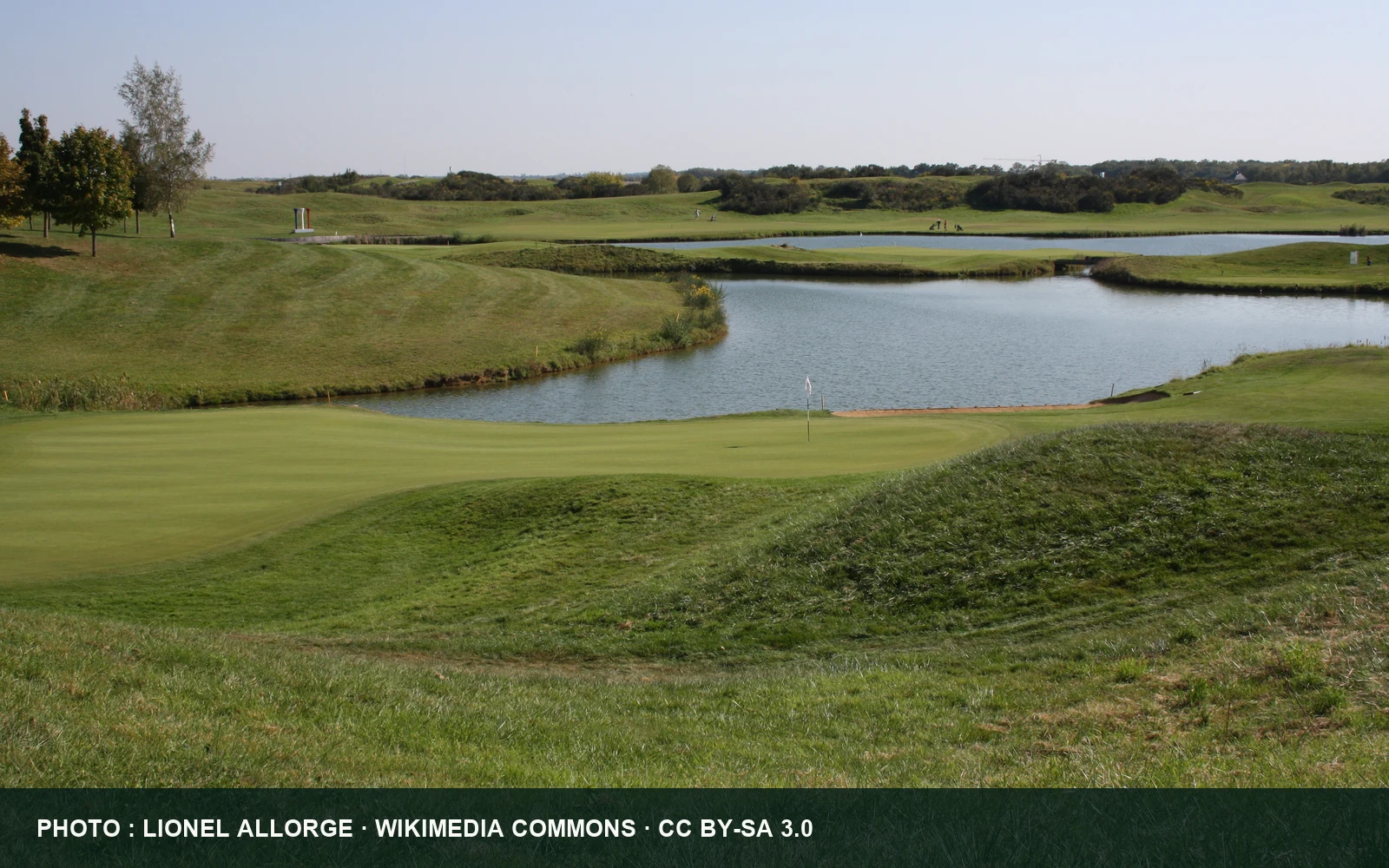 Vue du Golf National avec un green, une pièce d’eau et les ondulations du parcours.