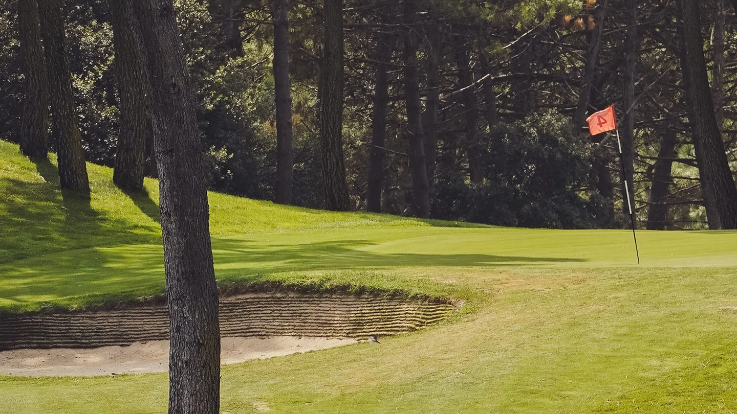 Green avec drapeau rouge et bunker au milieu des pins à La Palmyre Golf Club.