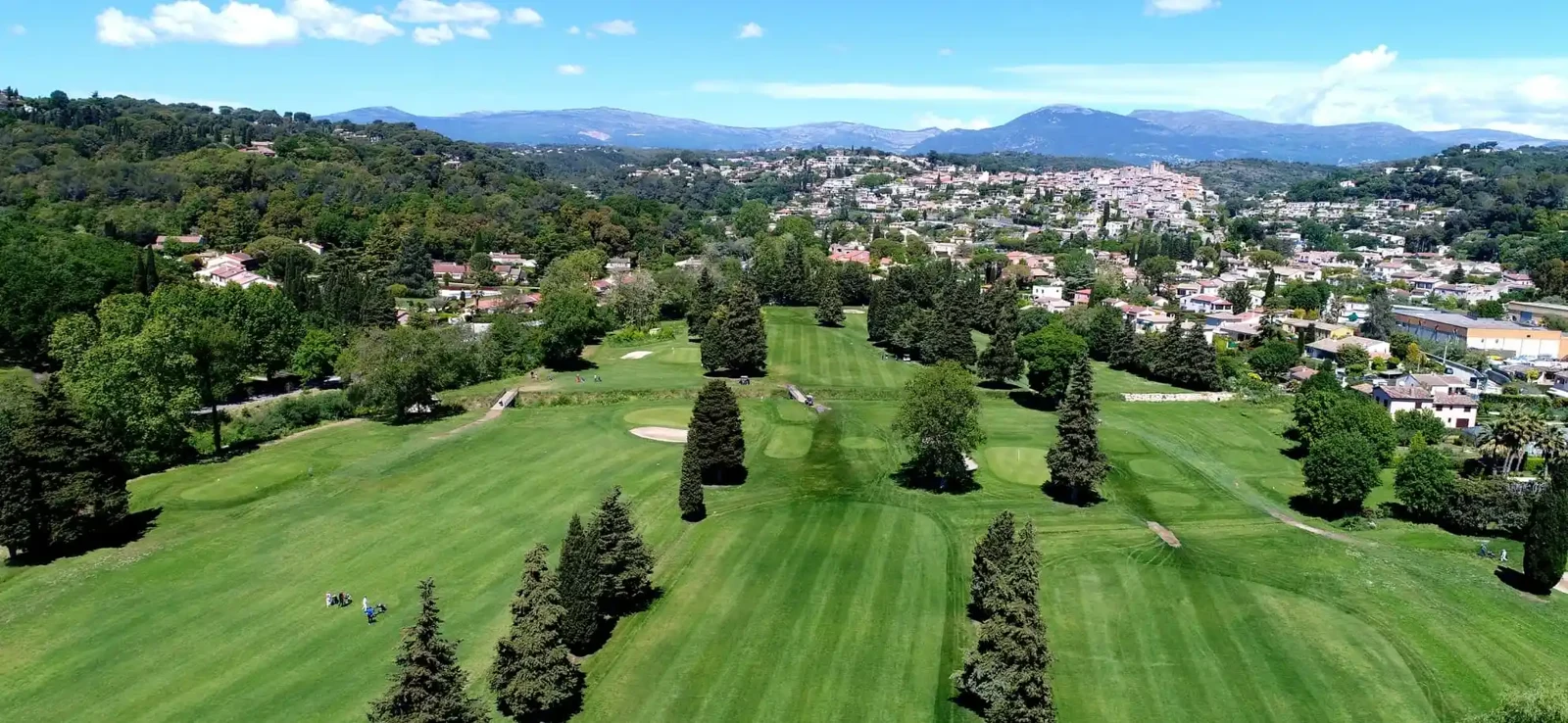 Vue aérienne des fairways bordés d’arbres et du village en arrière-plan.