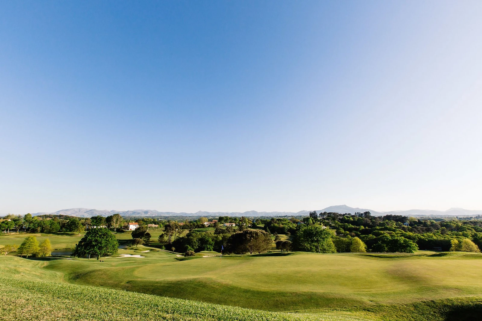 Vue du parcours vallonné du Golf d’Arcangues, avec un green au premier plan et les reliefs à l’horizon.