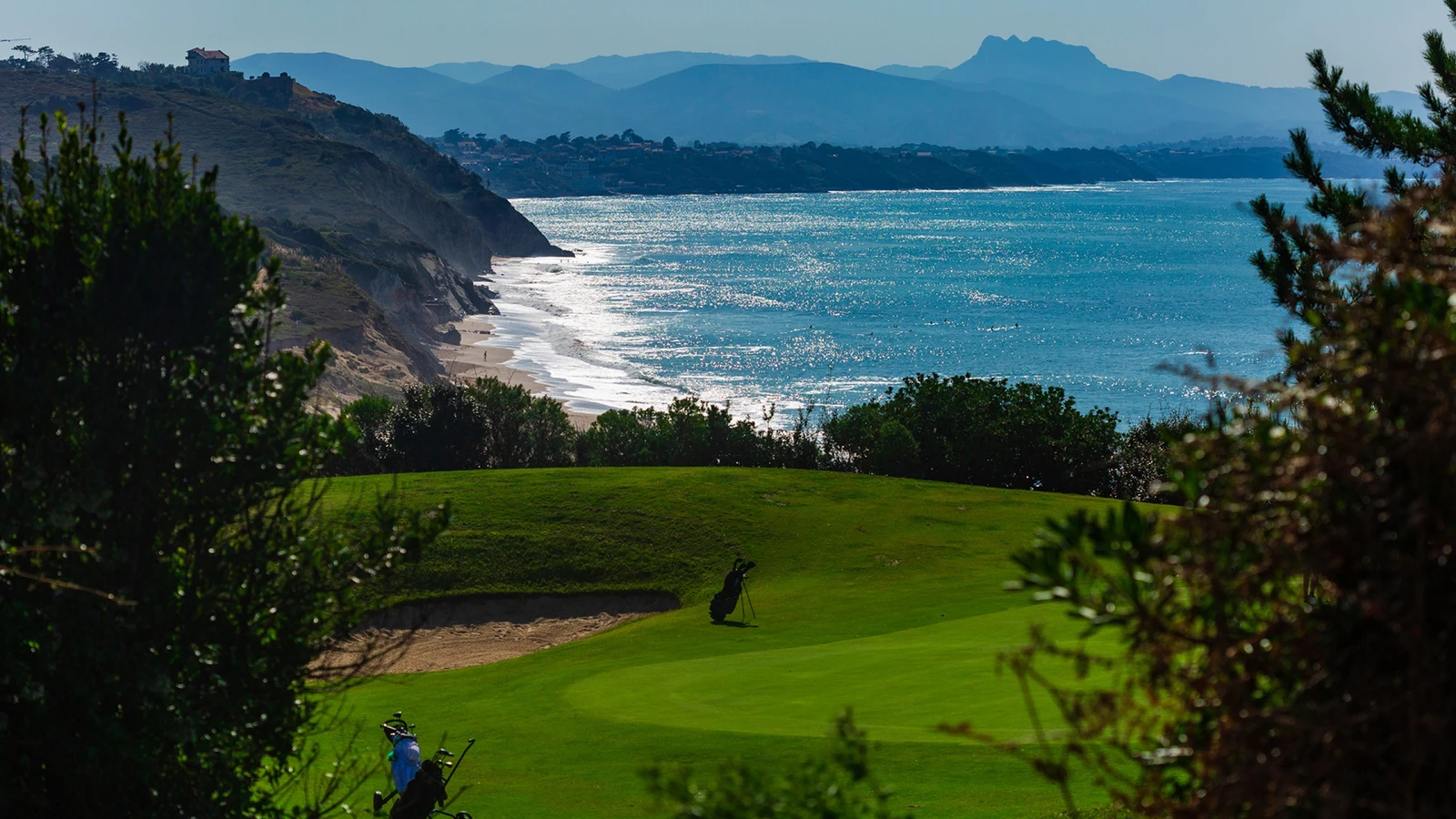 Golfeurs sur le parcours d’Ilbarritz, avec un bunker et la côte atlantique en arrière-plan.