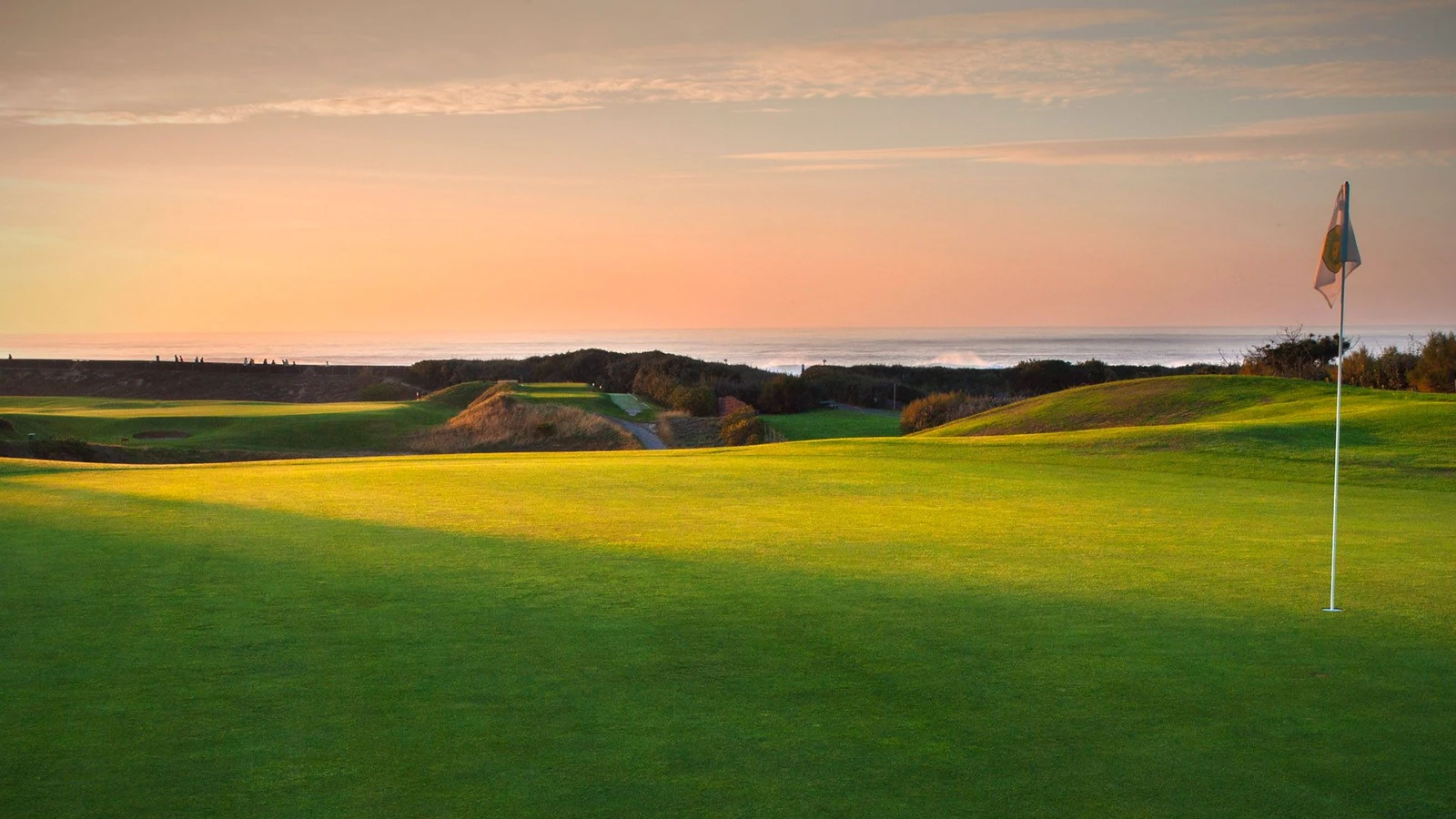 Green et drapeau du Golf de Chiberta, avec le rivage en arrière-plan sous un ciel orangé.