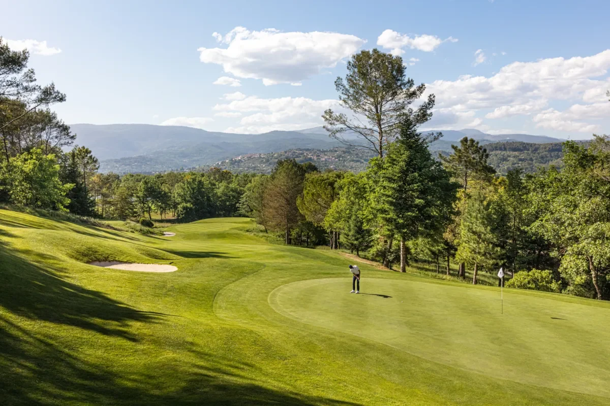 Golfeur sur le green du parcours Le Château à Terre Blanche, avec bunkers et collines boisées en arrière-plan.