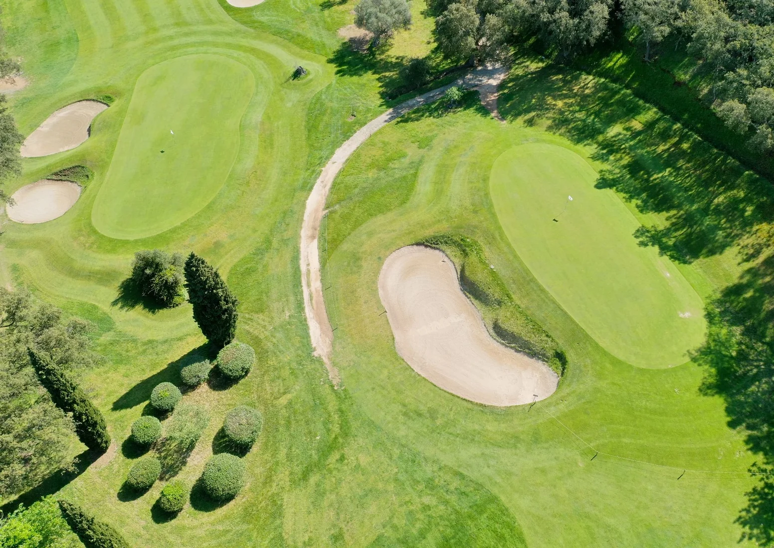 Vue aérienne de greens et bunkers du Golf de Valcros, bordés d’arbres et séparés par un chemin.