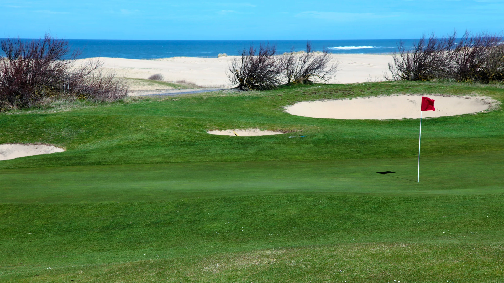 Green, bunker et drapeau rouge devant les dunes et l’océan au Golf de Moliets.
